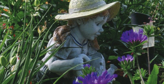 Statue of little girl wearing hat located in a garden